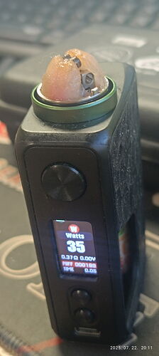 A black vape device is shown, its display reads 35 watts, and it has a coil and wicking material on top. (Labeled by AI)