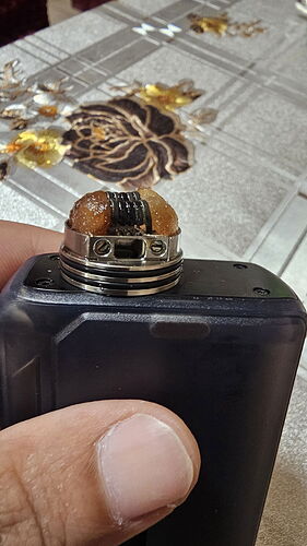 A képen egy kéz tart egy black vape modot, melyen egy használt coil és e-liquid maradványok láthatók. (Feliratozva AI-val)