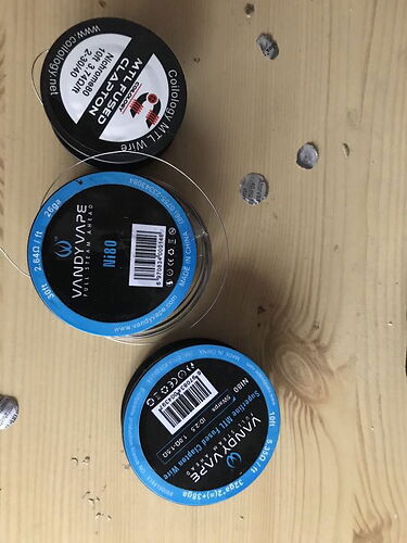 Three coils of unidentified wire on a wooden surface, two coils are Vandy Vape brand, and one is Coilology brand. (Caption by AI)