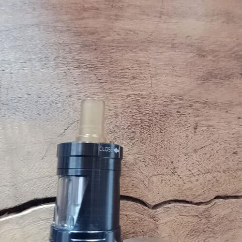 Un appareil de vape noir avec une partie supérieure transparente est visible sur une surface en bois. (Légendé par IA)