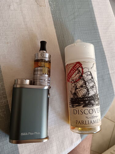 Une cigarette électronique et une bougie, sur lesquelles un navire et l'inscription "DISCOVER" sont visibles, sont placées sur une table. (Sous-titré par IA)