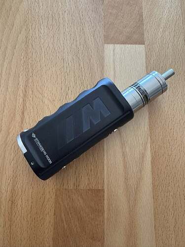 L'image montre une cigarette électronique noire et métallique, placée sur une surface en bois clair. (Légendé par l'IA)