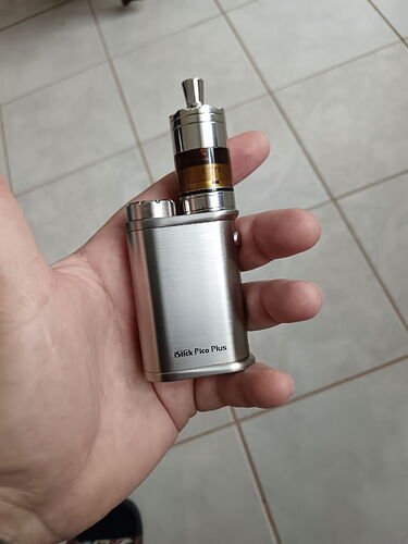 Une cigarette électronique (vape) argentée tenue dans une main, avec un sol carrelé clair en dessous. (Légendé par l'IA)