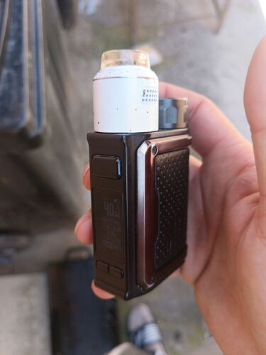 Un appareil vaporisateur tenu dans la main, avec écran numérique et partie supérieure blanche, est visible sur la photo. (légendé par IA)