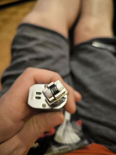 Egy férfi kezében lévő elektromos cigaretta (vape) fűtőtekercs része van éles fókuszban, miközben a háttérben az illető nadrágos lábai láthatók. (Feliratozva AI-val)