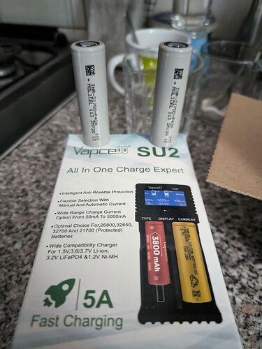 Two batteries and a Vapcell SU2 battery charger box are shown on a kitchen counter. (AI-generated caption)