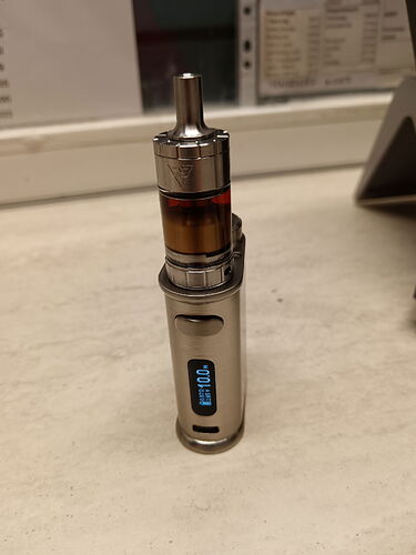A silver-colored electronic cigarette with a digital display stands on the table. (Subtitled with AI)