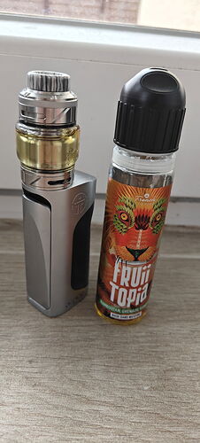 Az image két vapelni való eszközt ábrázol: egy ezüst színű modot és egy színes ízesítésű folyadékot, melyen egy oroszlán látható. (Feliratozva AI-val)