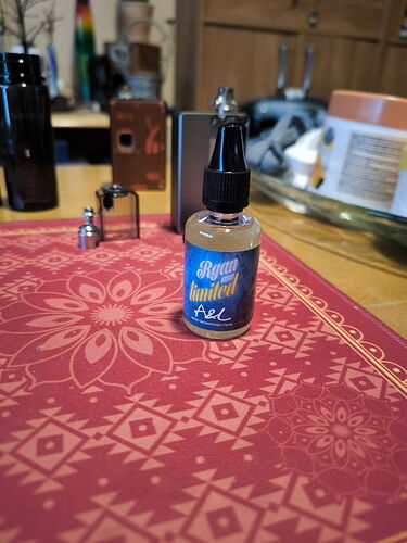 In the picture, a bottle of e-liquid is visible, bearing the inscription "Ryum United", and it is placed on a colorful dark red patterned coaster. (Captioned by AI)