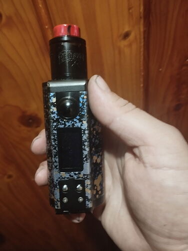 A hand holds an electronic cigarette with a patterned design featuring black and red elements against a wooden background. (Captioned by AI)