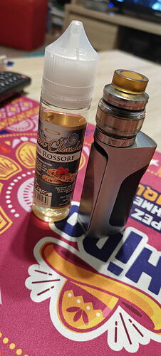 Egy vape készülék és egy e-liquid palack látható egy színes, mintás alátéten. (Feliratozva AI-val)