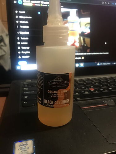 The image shows a white plastic bottle which features the text "BLACK CAVENDISH" and the "LA TABACCHERIA" logo, while a laptop keyboard is also visible in the background. (Labeled by AI)