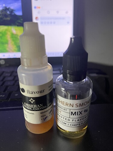 Két e-liquid flakon áll egy laptop előtt, egyik fehér kupakkal, másik fekete kupakkal. (Feliratozva AI-val)