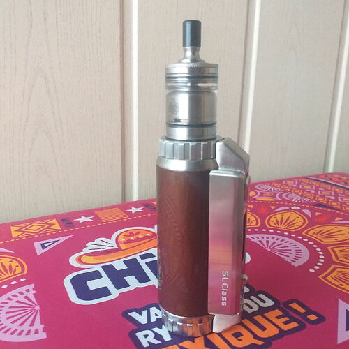 Un mod de vape en métal et bois est placé sur une table colorée. (Légendé par l'IA)