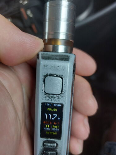 A hand holds a gray e-cigarette, on whose display 11.7W is visible. (Labeled by AI)