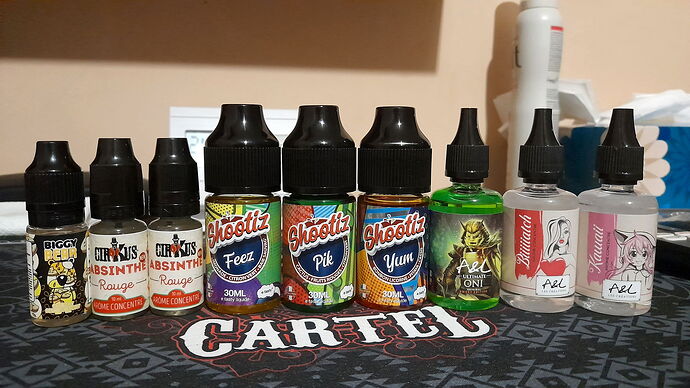 Sur la table, divers flacons d'e-liquide sont alignés devant un sous-bock "CARTEL". (Légendé par IA)
