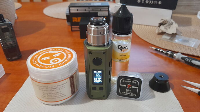 Various e-cigarette accessories, e-liquid, and coils are visible on the table next to a green e-cigarette device. (Subtitled by AI)