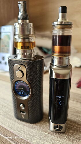 Két különböző elektromos cigaretta (vape) készülék áll egy asztalon. (Feliratozva AI-val)