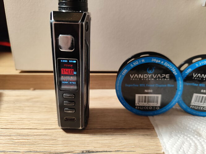 A black e-cigarette device is visible on a table, next to it are two boxes of coils made by Vandy Vape, containing 0.19 ohm resistances. (Subtitled by AI)
