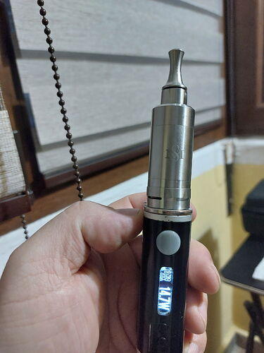 Egy kéz egy digitális kijelzős és gombos elektromos cigarettát (vape) tart egy ablak előtt. (Feliratozva AI-val)