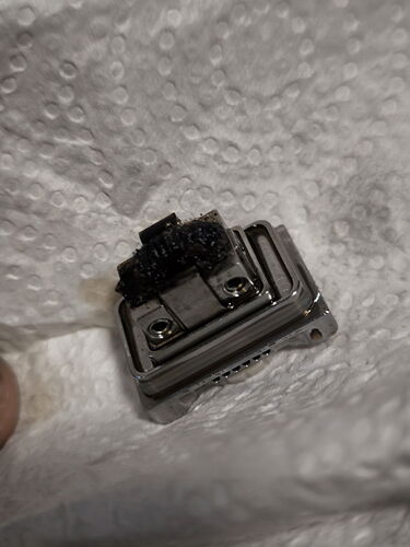 Une pièce métallique sale est visible avec une saleté noire et poilue sur le dessus, sur une surface blanche texturée. (Légendé par IA)