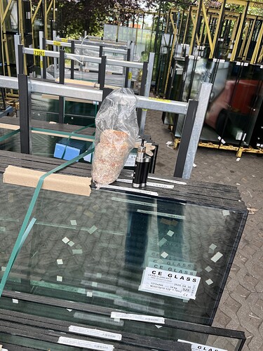 The glass sheets are located on a storage rack outdoors, with various wooden and metal structures visible around them. (Labeled by AI)