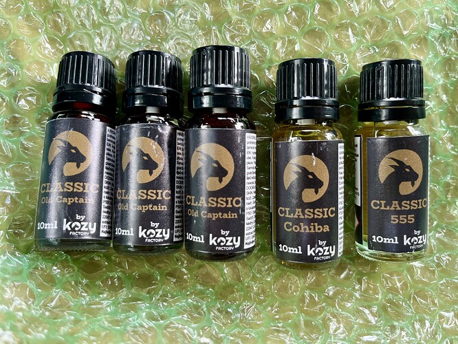 Les cinq flacons d'e-liquide de marque Classic en format 10 ml, dans différentes variations (Captain, Cohiba, 555), reposent sur du papier bulle. (Légendé par IA)