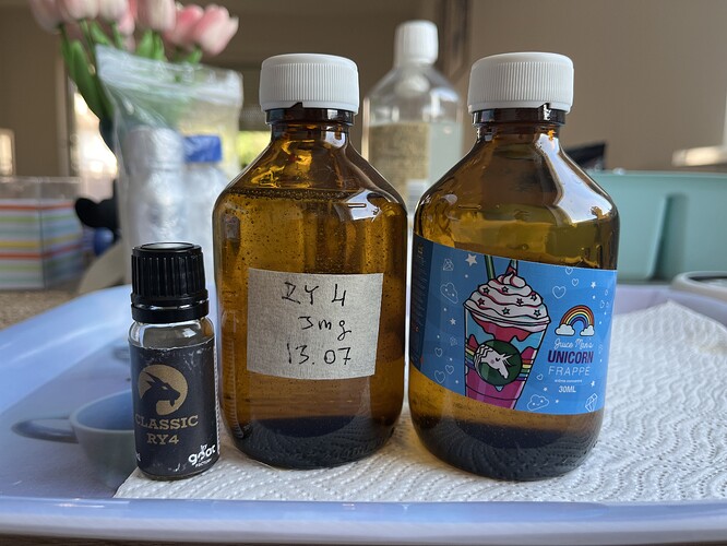 Three different sized brown bottles, one with a handwritten label, another has a drawn unicorn label, and a small black bottle is next to them on a tray in a kitchen background. (Labeled by AI)