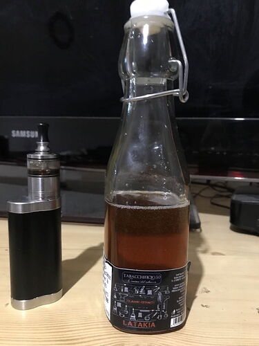 Az asztalon egy üveg sötétbarna folyadékkal és egy elektronikus cigarettával találkozunk, háttérben egy tévé látható. (Feliratozva AI-val)