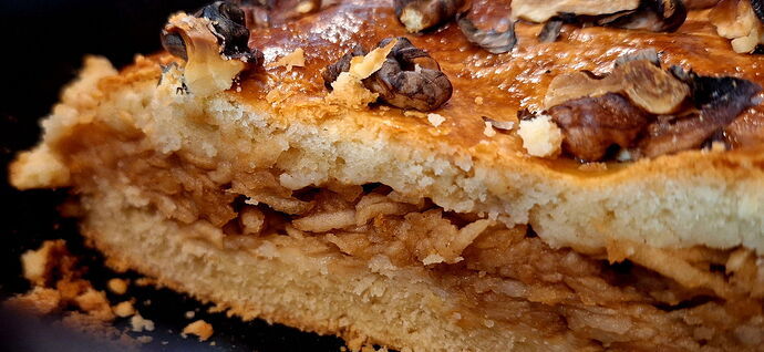 Cette image montre une part de tarte aux pommes faite maison, garnie de noix. (Sous-titré par IA)