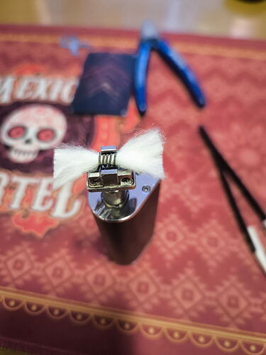 Egy öngyújtó lángterelővel és gyapjúból készült vattával a tetején, asztalon szerszámokkal háttérben. (Feliratozva AI-val)