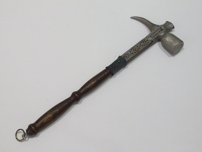 Une hache ou un marteau en métal avec un manche en bois sculpté et décoré est visible sur l'image. (Légendé par IA)